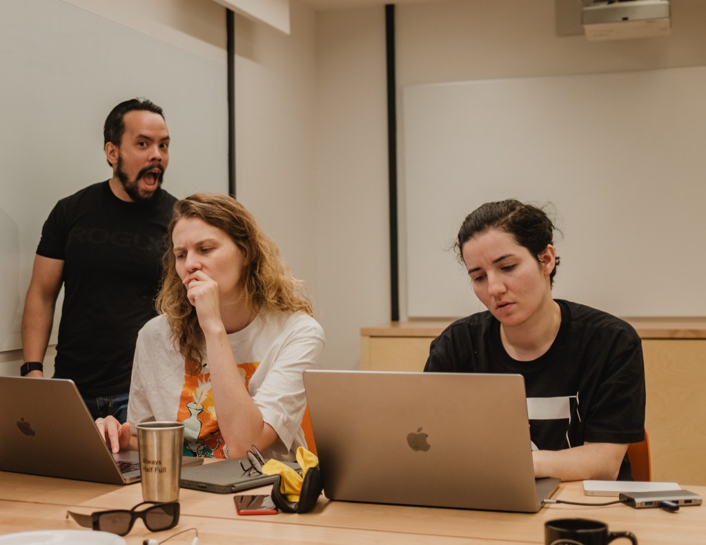 Two software engineers focused on their laptops with a manager supervising.